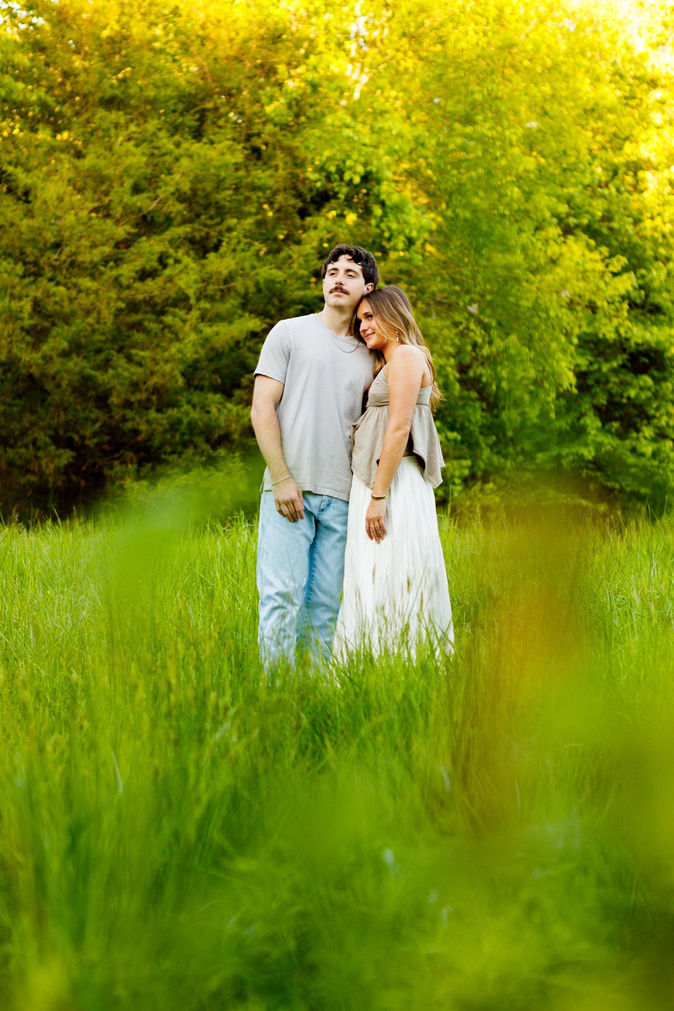 A couple stands together in tall green grass