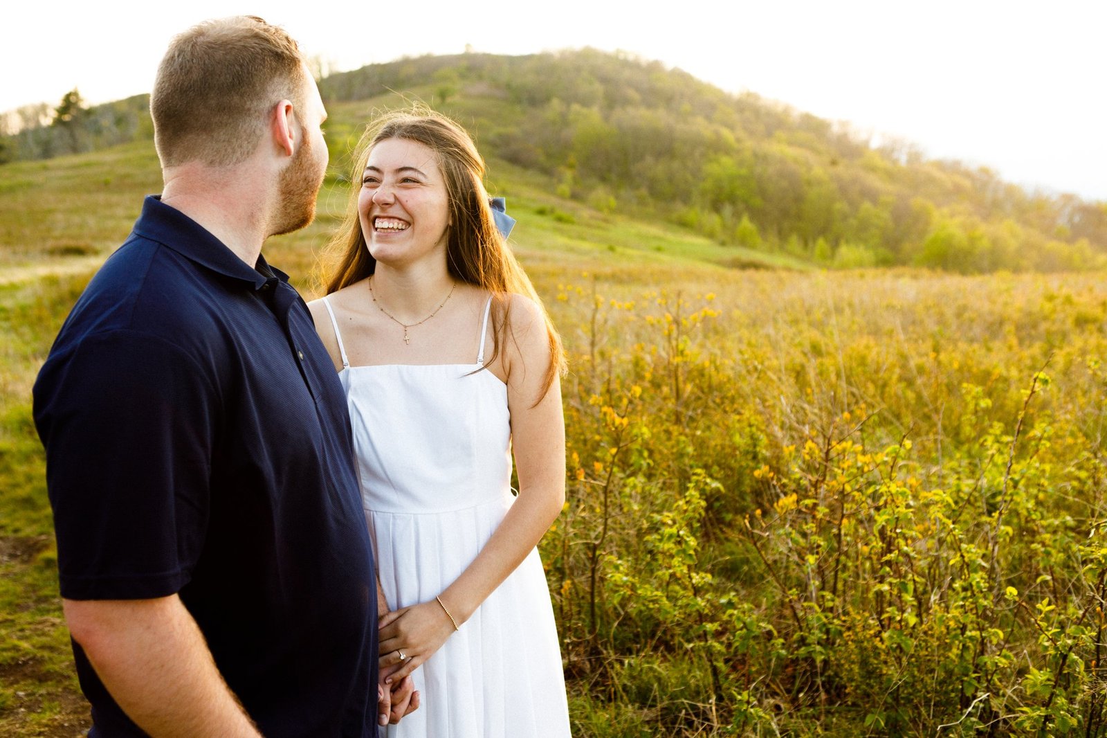 A couple smiles together in a sunlit meadow