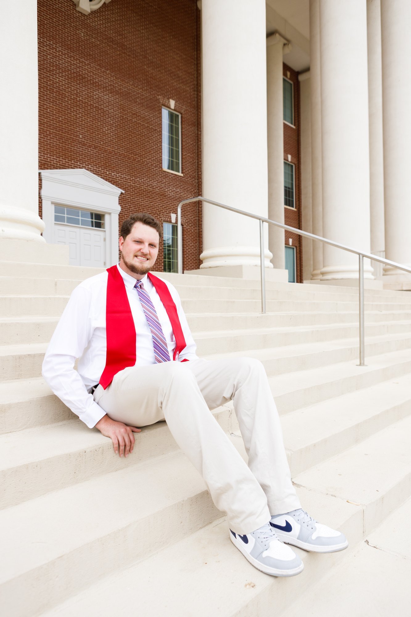 A graduate sits on the steps outside a campus building