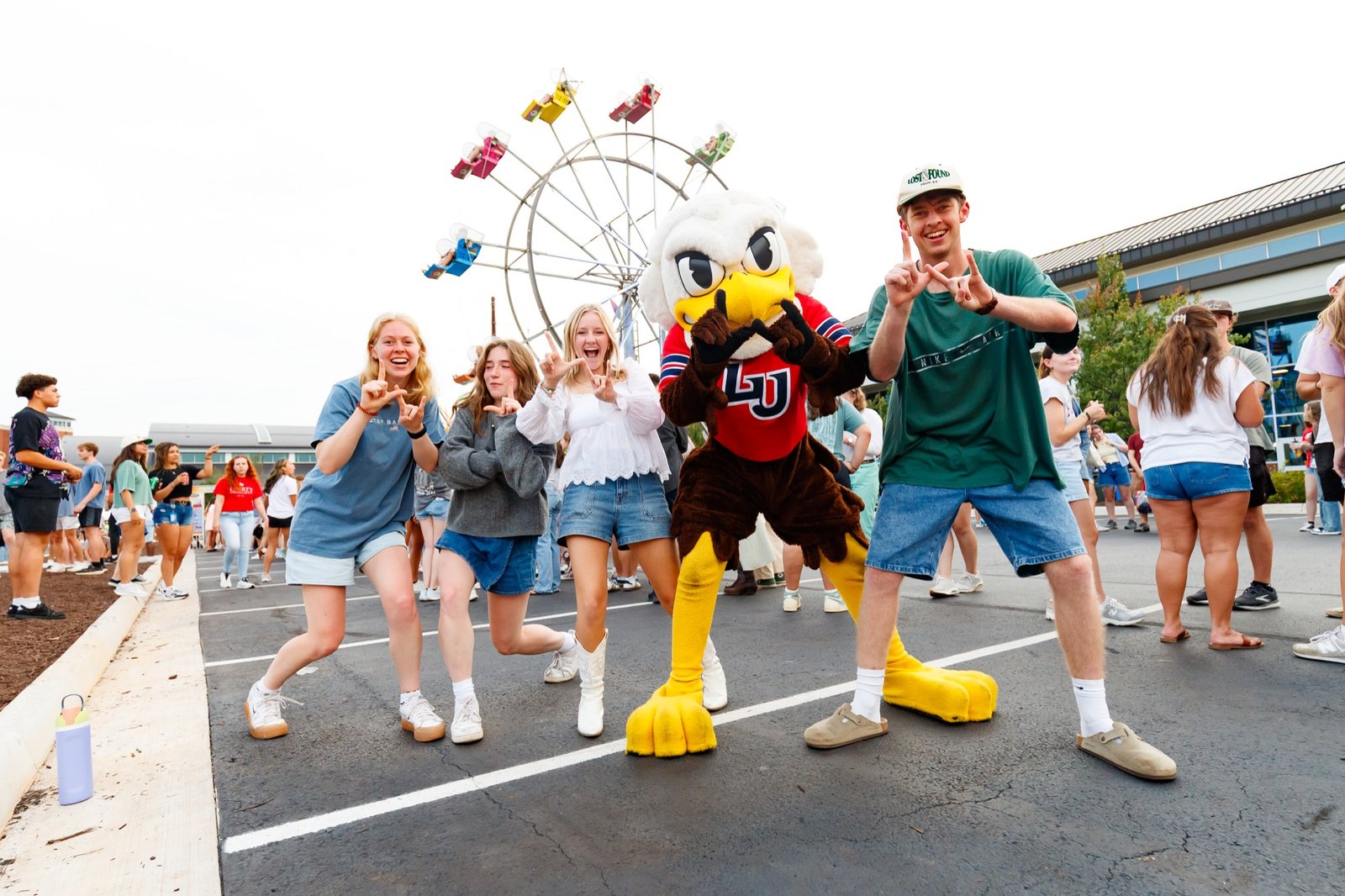 Students and the Liberty mascot pose near the carnival rides