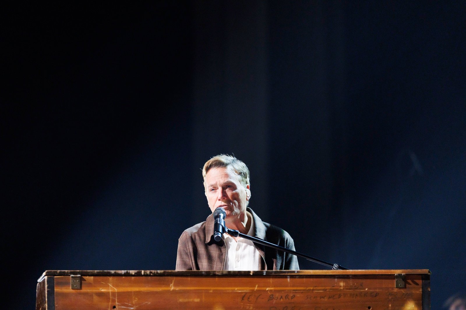 A musician performs at a keyboard against a dark stage