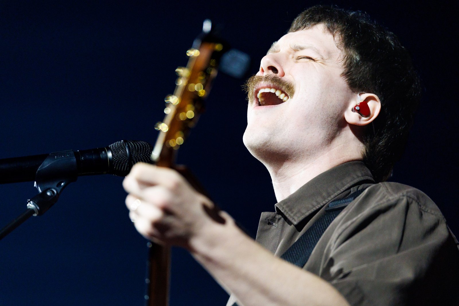 A singer performs with a guitar under stage lights