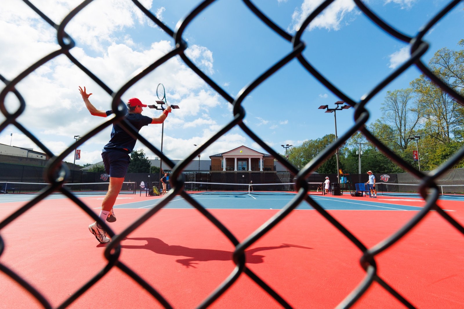 A tennis player seen through the court fence