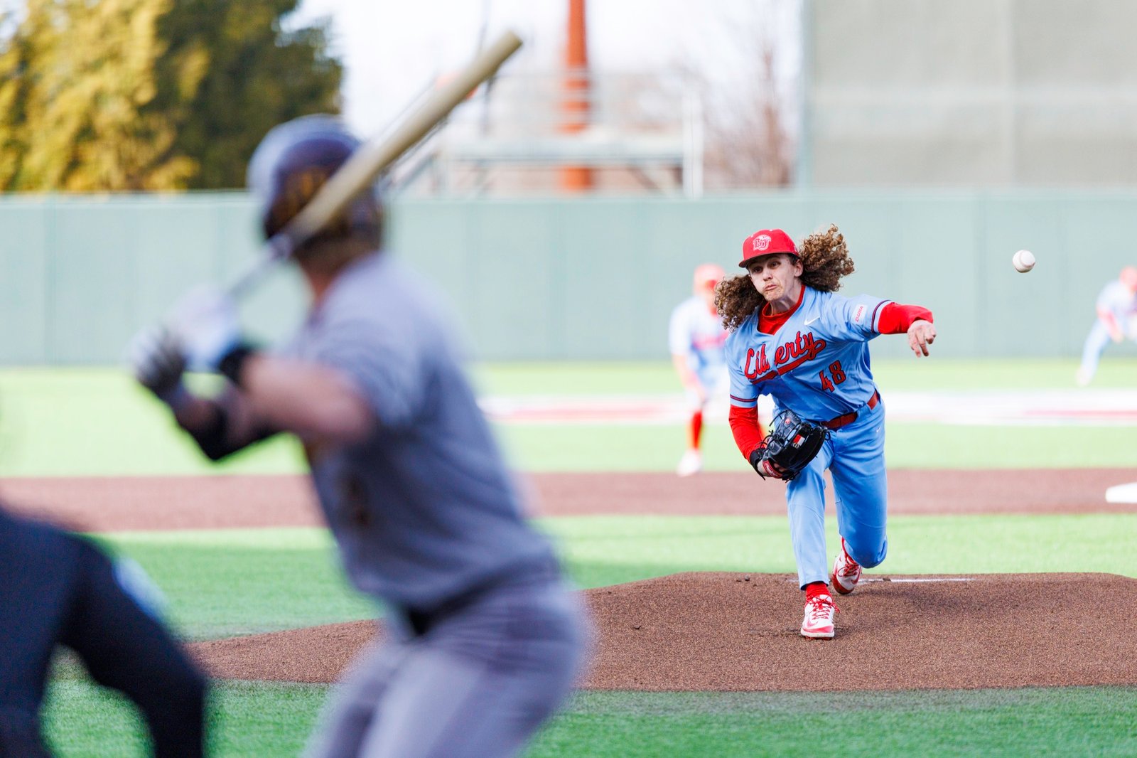 A baseball pitcher delivers the ball past a foreground batter